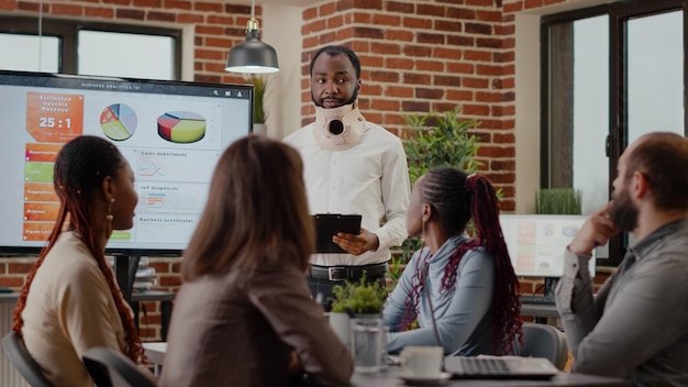 Injured employee in pain wearing neck collar at business job, presenting strategy. Man using medical cervical foam after accident to heal ache from fractured vertebrae and injury.