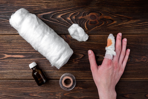 Injured painful finger with white gauze bandage on dark wooden table.