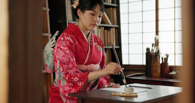 Foto scrittura a inchiostro e donna giapponese tradizionale a casa per la scrittura su documenti cartacei e pagine cultura creativa asiatica e persona con strumenti di pennello vintage per la calligrafia carattere e testo in casa