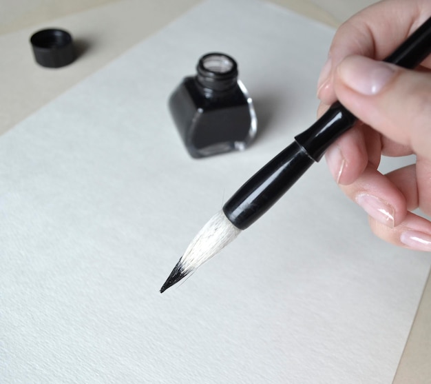 Foto inktfles met penseel in de hand voor het tekenen van chinese schilderkunst op wit