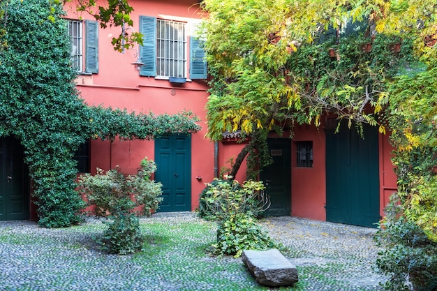 The inner courtyard of the house with a red house wall overgrown with green plants and a bench in th