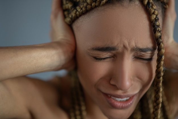 Foto dolore interiore. giovane donna afroamericana frustrata che soffre, accigliata, coprendosi le orecchie con le mani