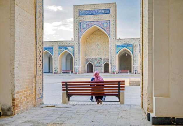 Inner yard of Kalyan Mosque part of the PoiKalyan Complex at the sunset Bukhara Uzbekistan A woman in a headscarf sitting on the bench