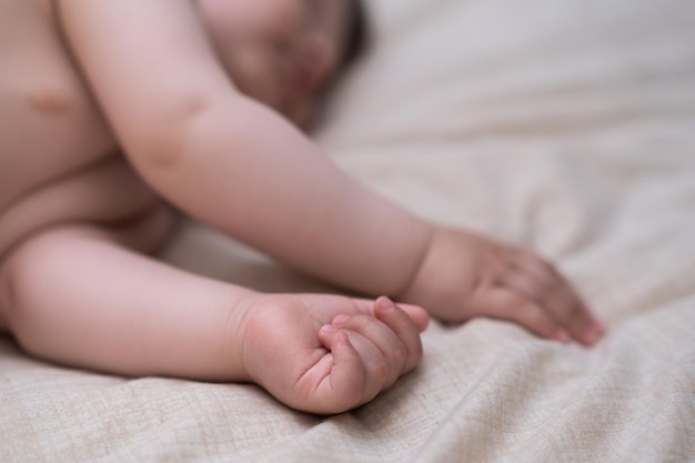 Innocent little boy sleeping in crib grabbing soft white sheet with tiny hands