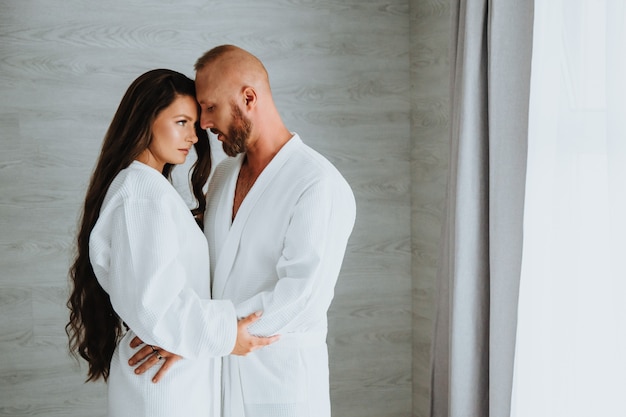 Inschrijving en een mooi jong verliefd stel in witte badjassen in het luxehotel of de slaapkamer staan en omhelzen elkaar. Gelukkig samen