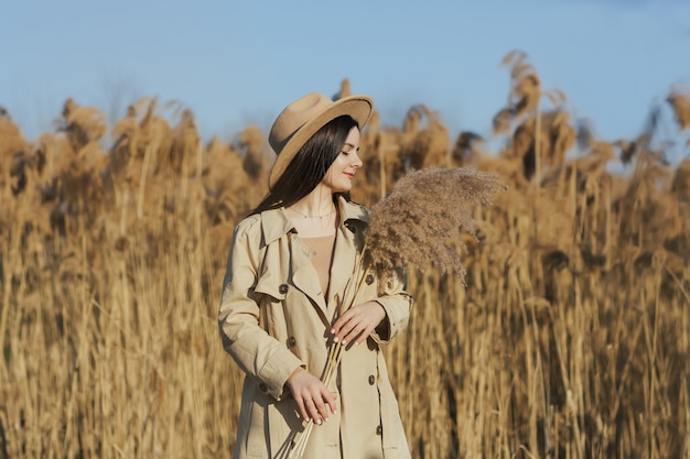 Inschrijving en mooi meisje met gesloten ogen in beige trenchcoat en hoed met boeket van pampagras