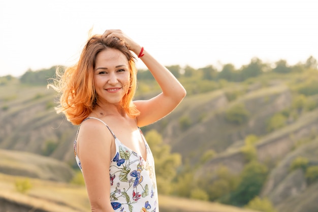 Inschrijving mooie roodharige vrouw geniet van de zonsondergang in een veld met een heuvel.