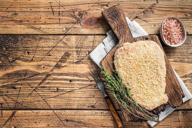 Inschrijving rauwe gepaneerde Wiener schnitzel op een houten bord met tijm. houten achtergrond. Bovenaanzicht. Ruimte kopiëren.