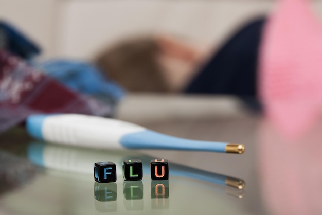 Inscriptie FLU-thermometer en zakdoeken op de wazige achtergrond van een ziek meisje dat in bed ligt