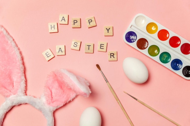 Inscriptie happy easter letters eieren kleurrijke verf en bunny oren geïsoleerd op trendy roze achtergrond