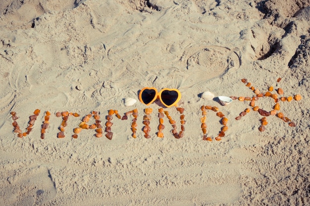 Inscriptie vitamine D met vorm van zon en zonnebril op zand op strand Preventie van vitamine D-tekort Zomer- en vakantietijd