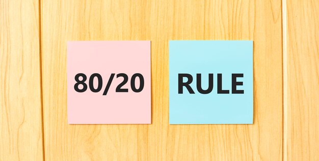 写真 80-20 ルールは木製の壁に貼り付けられたピンクとブルーの正方形のステッカーに書かれています