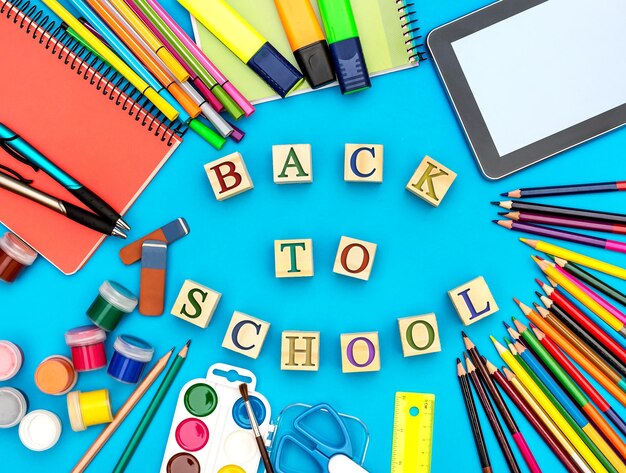 Inscription Back to school by wooden cubes with school supplies on blue background Top view