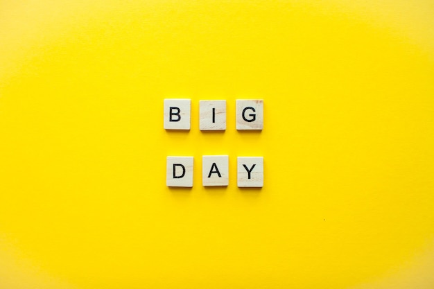 Photo the inscription big day from wooden blocks on a bright yellow background