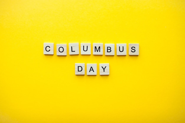 Photo the inscription columbus day from wooden blocks on a bright yellow background