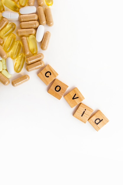 Inscription COVID in wooden cubes on a white background of different pills