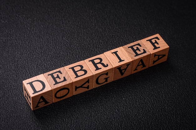 The inscription debrief in wooden cubes on a dark concrete background