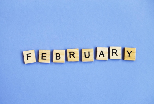 Inscription February made by wooden cubes on a veri peri purple background