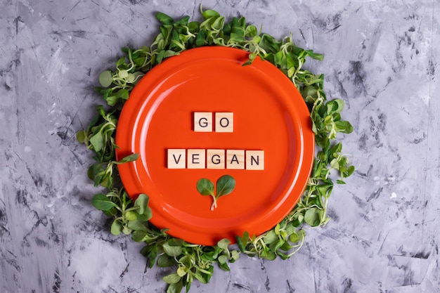 Inscription go vegan letters on an orange plate in a frame of green fresh corn salad