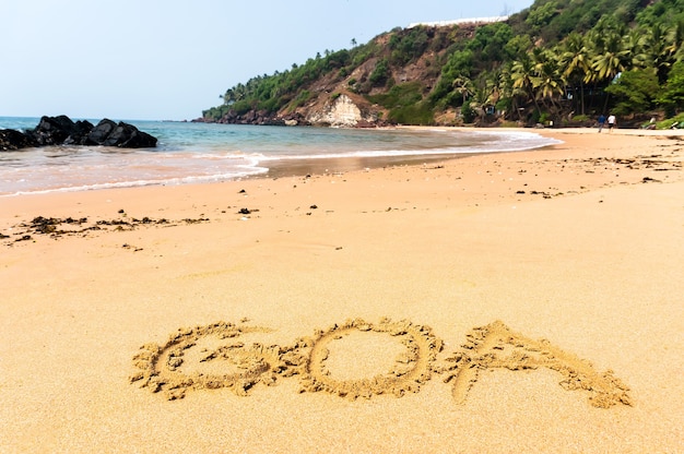 The inscription goa on a sandy beach against the blue sea and the turquoise water and waves