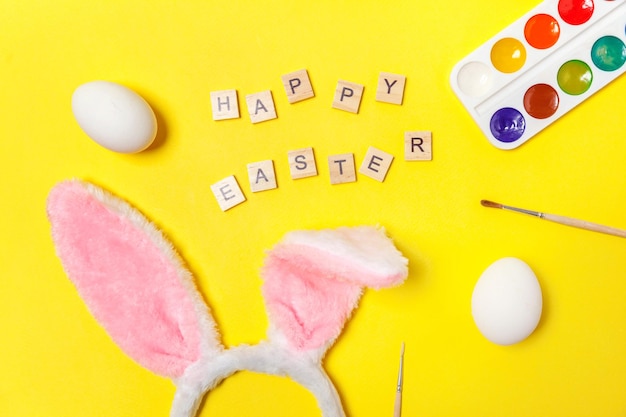 Inscription happy easter letters eggs colorful paints and bunny ears isolated on trendy yellow backg...