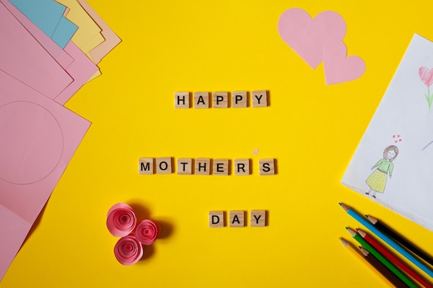 inscription happy womens day lined with wooden letters Flat lay Childish drawing for mothers day next to pencils