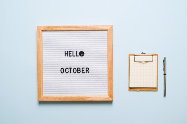 Inscription Hello October on white letter board, with dry leaves over light blue background. Autumn concept