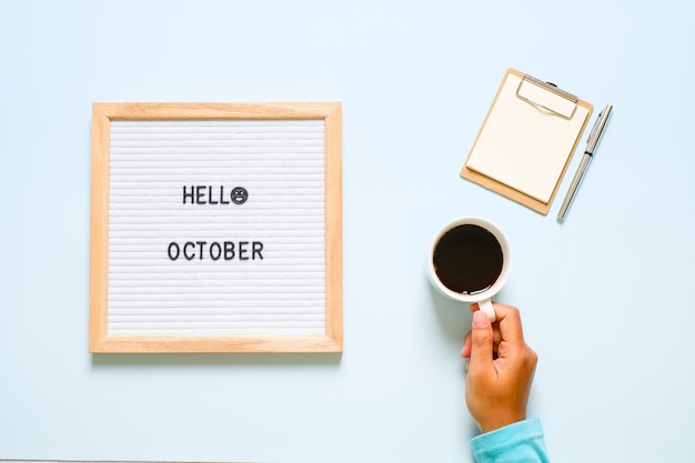 Inscription hello october on white letter board, with dry\
leaves over light blue background. autumn concept