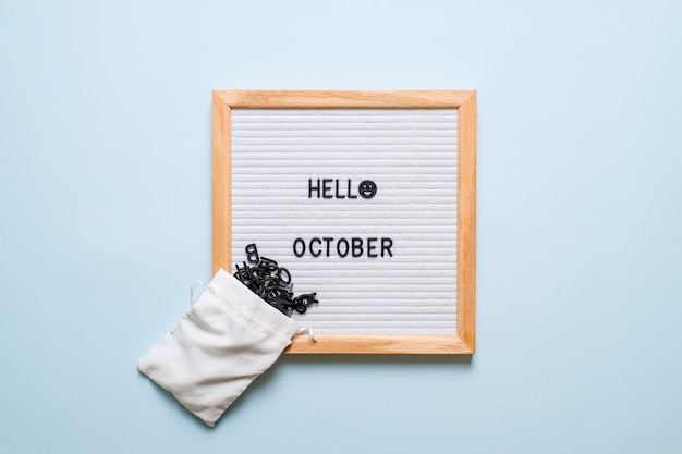 밝은 파란색 배경 위에 마른 잎이 있는 흰색 문자판에 Hello October라는 글자가 새겨져 있습니다. 가을 컨셉