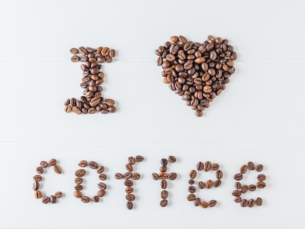 The inscription i love coffee written by roasted coffee beans on a white wooden table. the view from the top. flat lay. grains for the preparation of the popular drink.