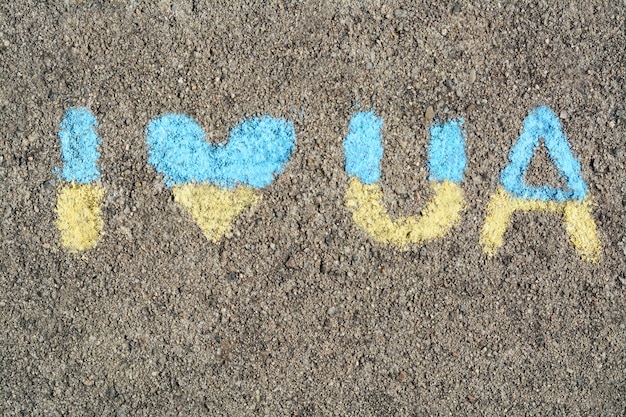 Inscription I love Ukraine drawn by blue and yellow chalk on asphalt top view