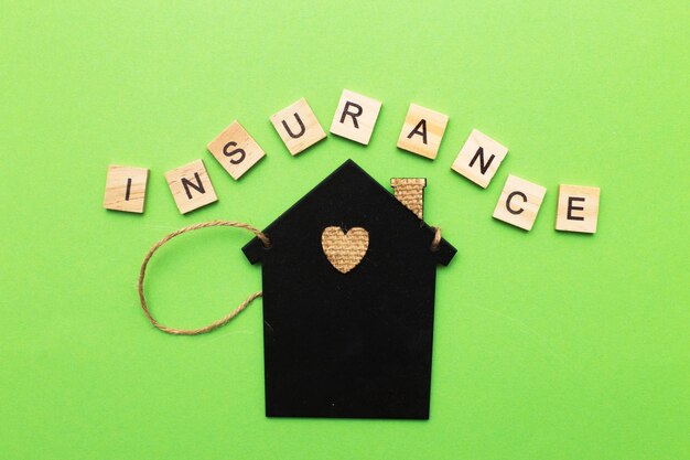 Inscription insurance with a little house on a green background made by wooden blocks.