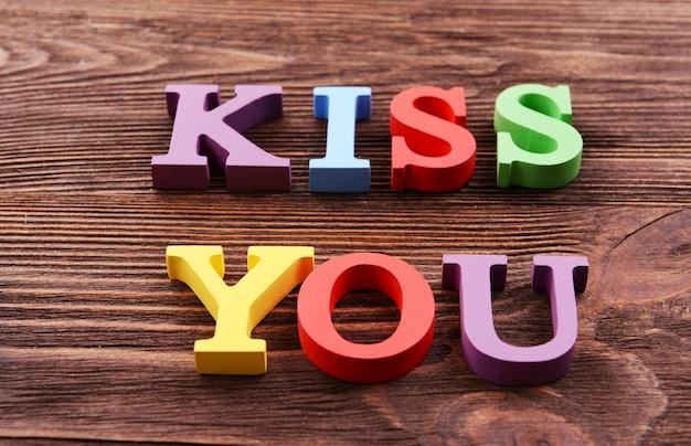 Photo inscription kiss you made of colorful letters on wooden background