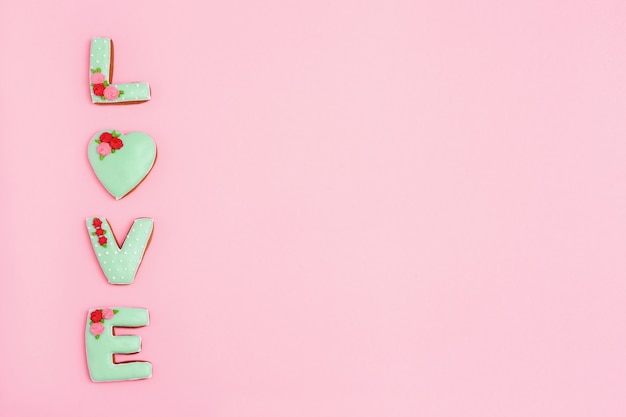 Inscription Love by homemade cookies on pink background with copy space. Holiday concept for wedding or Valentines Day.  Minimal style composition.