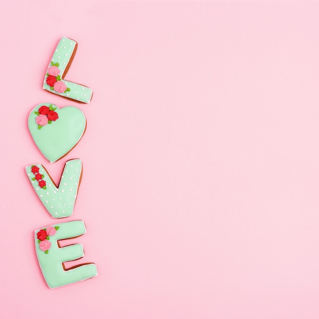 Inscription Love by homemade cookies with green icing on pink pastel color. Love romance concept. Valentines Day View from above.