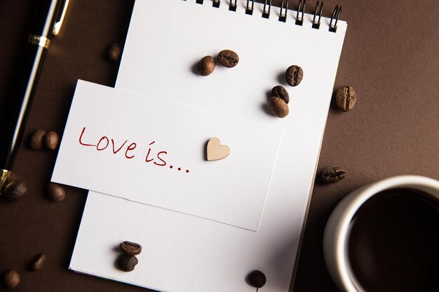 The inscription love is and a notebook with a cup of coffee