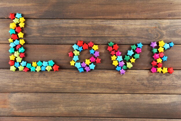 Inscription LOVE made of p decorative paper stars on wooden background