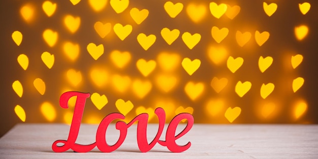 The inscription Love on a wooden background with beautiful hearts made of lights on a blurred background