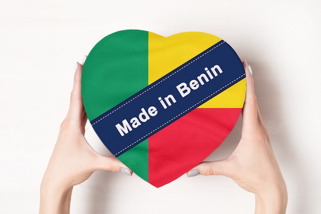 Inscription Made in Benin the flag of Benin. Female hands holding a heart shaped box.