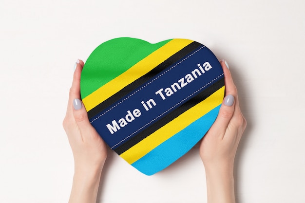 Inscription Made in Tanzania the flag of Tanzania. Female hands holding a heart shaped box