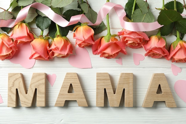 Inscription Mama with pink roses, ribbon and little hearts on wooden table, top view