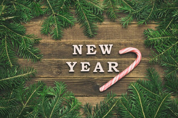 Inscription Merry Xmas on a wooden background Frame of fir branches and candy stick