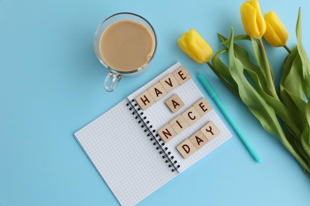 Inscription in the notebook have a good day coffee and yellow tulips on a blue background