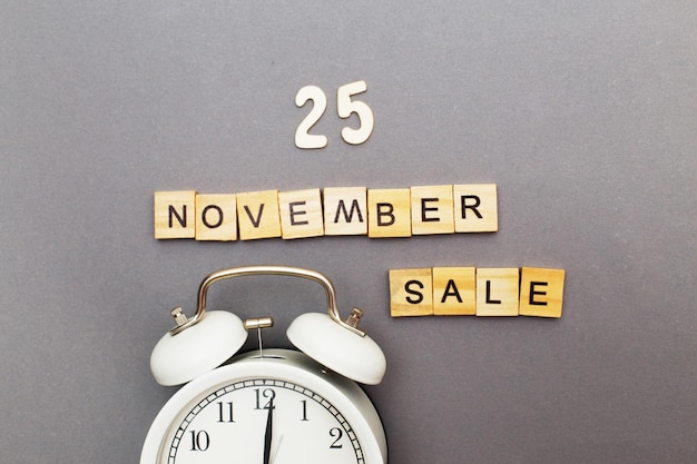 Надпись 25 ноября продажа деревянных кубиков и будильник на сером фоне