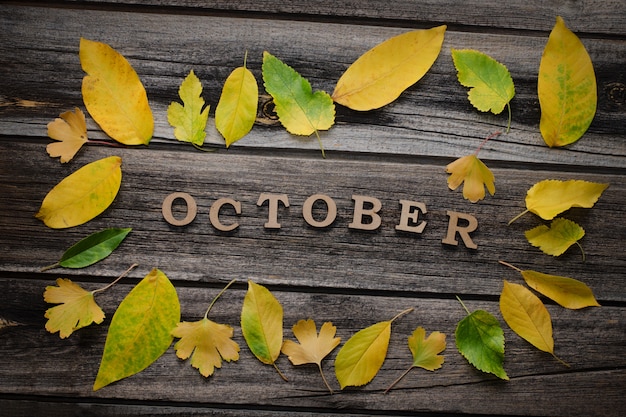 Inscription October on a wooden background with frame of yellow leaves