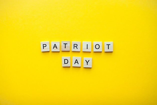 Photo the inscription patriot day from wooden blocks on a bright yellow background