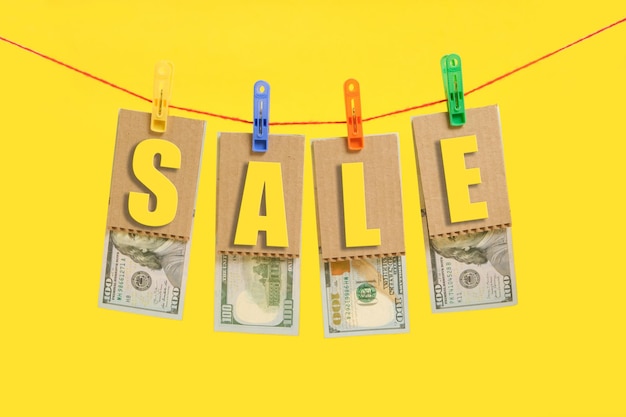 Photo inscription sale with hundred dollar bills is hung on clothespins on yellow background