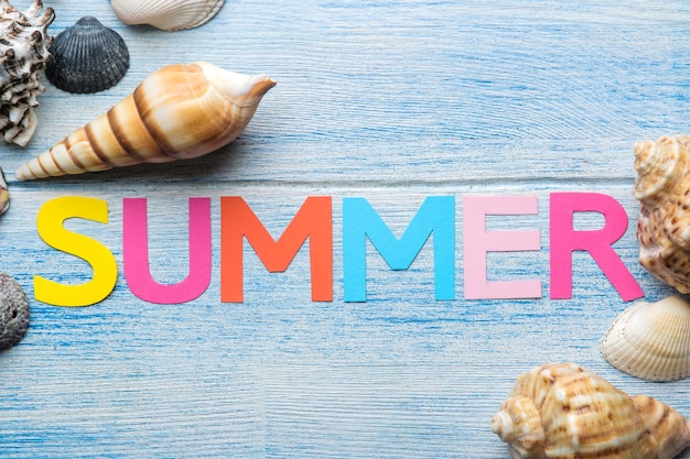 青い木製のテーブルに色とりどりの文字と貝殻と夏と海のアクセサリーの紙からの碑文の夏。夏。リラクゼーション。休暇。上面図