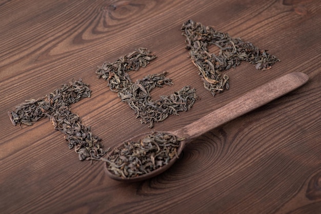 Inscription Tea on black wooden table spoon beneath Concept of black tea