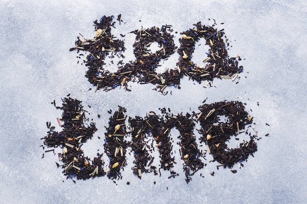 Inscription Tea of dry tea leaves and flowers on a gray background.